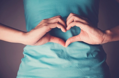 A person making a heart shape over their stomach with their hands.