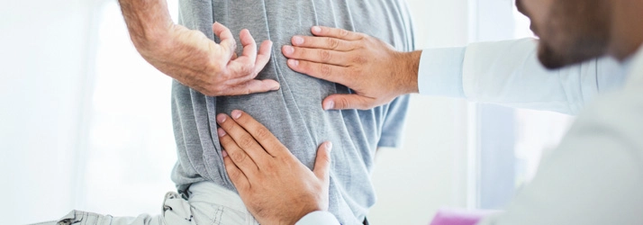 A person pointing to their middle back, while a chiropractor looks.