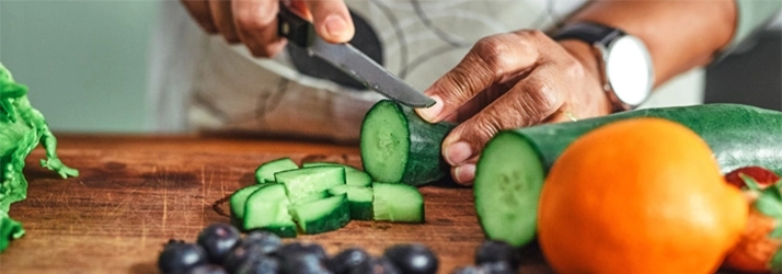 A person chopping a cucumber on a wooden cutting board.