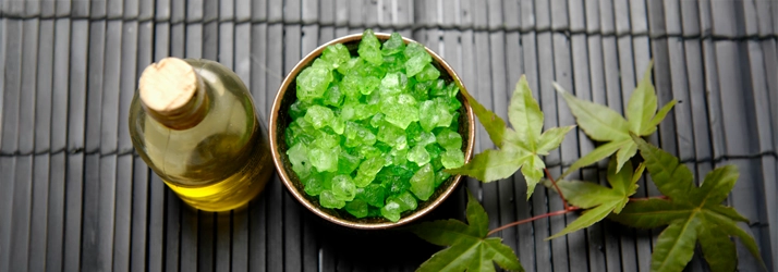 A bottle of oil sitting next to green salt rocks.